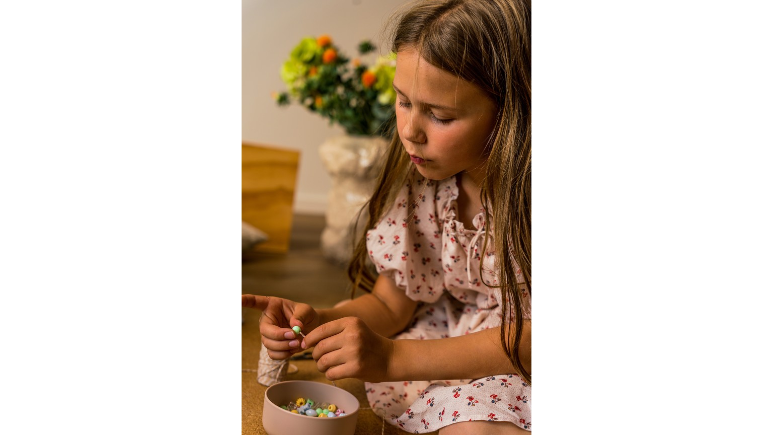 Barn med hvid kjole sidder ved bord og leger med små perler og et mønsterbræt